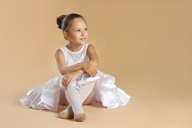 Portrait of little ballerina on beige background, space for text