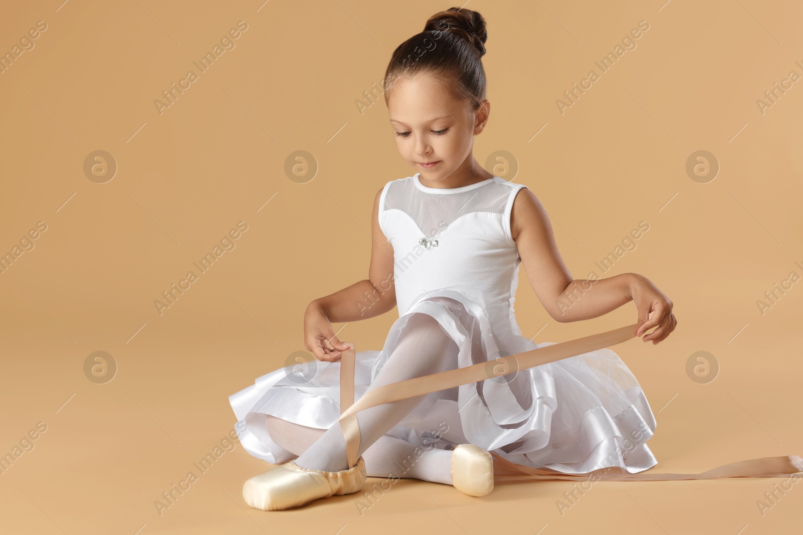 Photo of Little ballerina tying pointe shoes on beige background