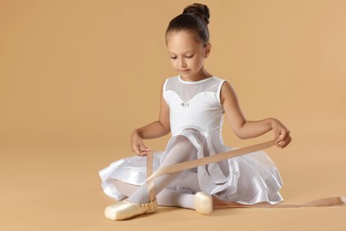 Little ballerina tying pointe shoes on beige background