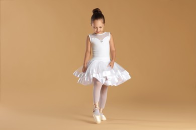 Photo of Little ballerina practicing dance moves on beige background