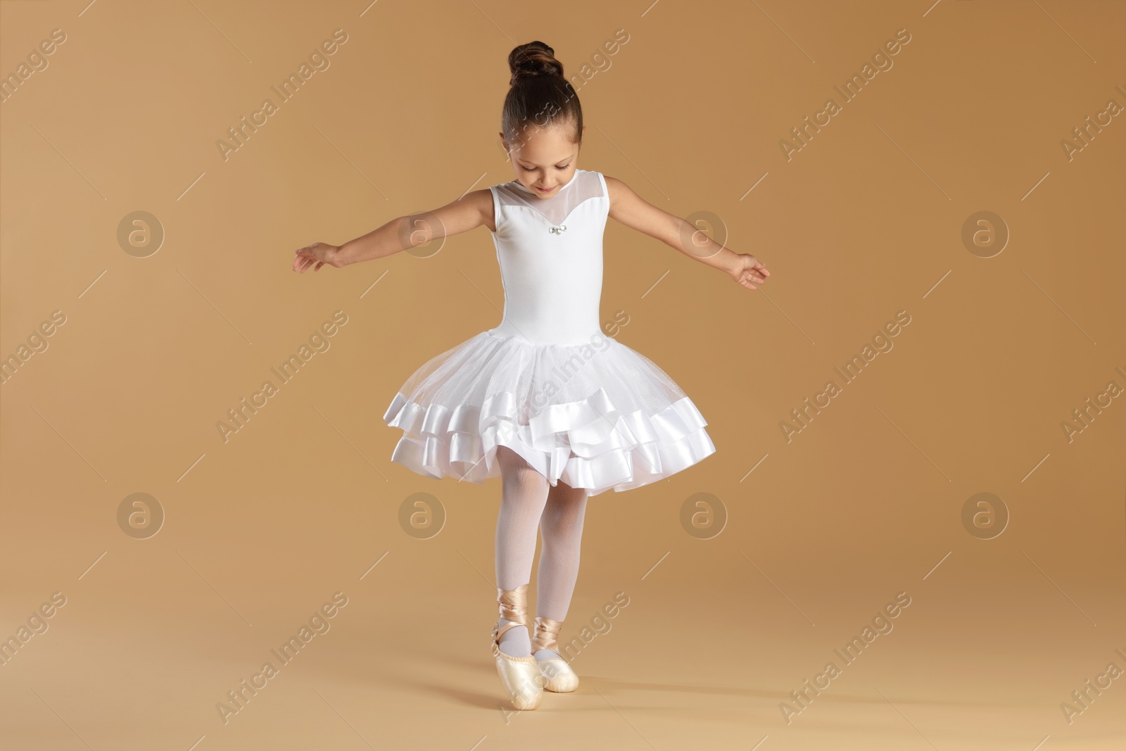 Photo of Little ballerina practicing dance moves on beige background