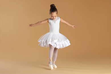 Little ballerina practicing dance moves on beige background