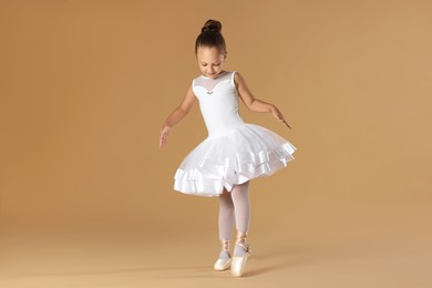 Little ballerina practicing dance moves on beige background