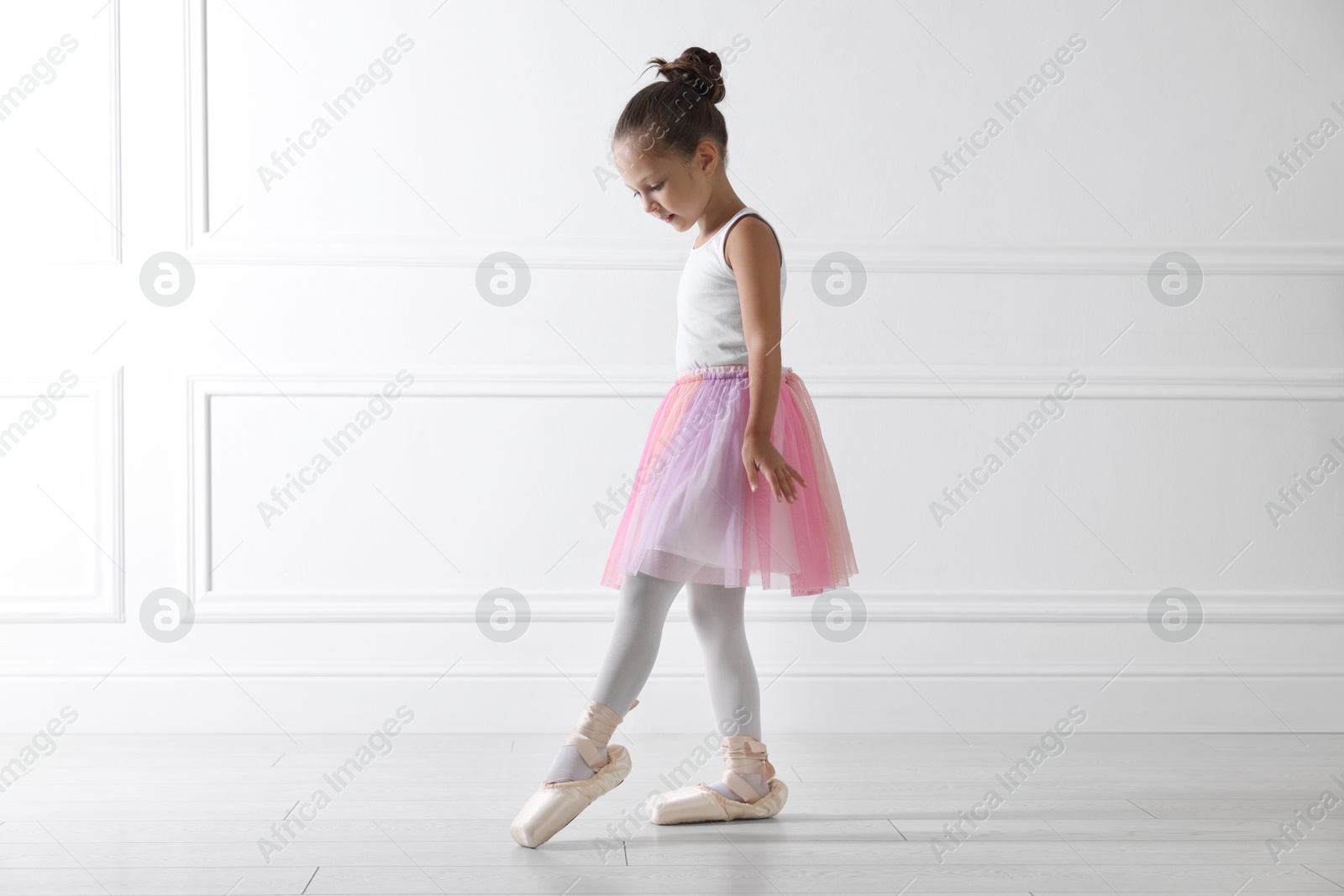 Photo of Little ballerina practicing dance moves near white wall indoors