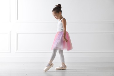 Photo of Little ballerina practicing dance moves near white wall indoors