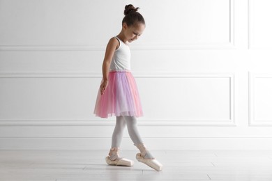 Photo of Little ballerina practicing dance moves near white wall indoors