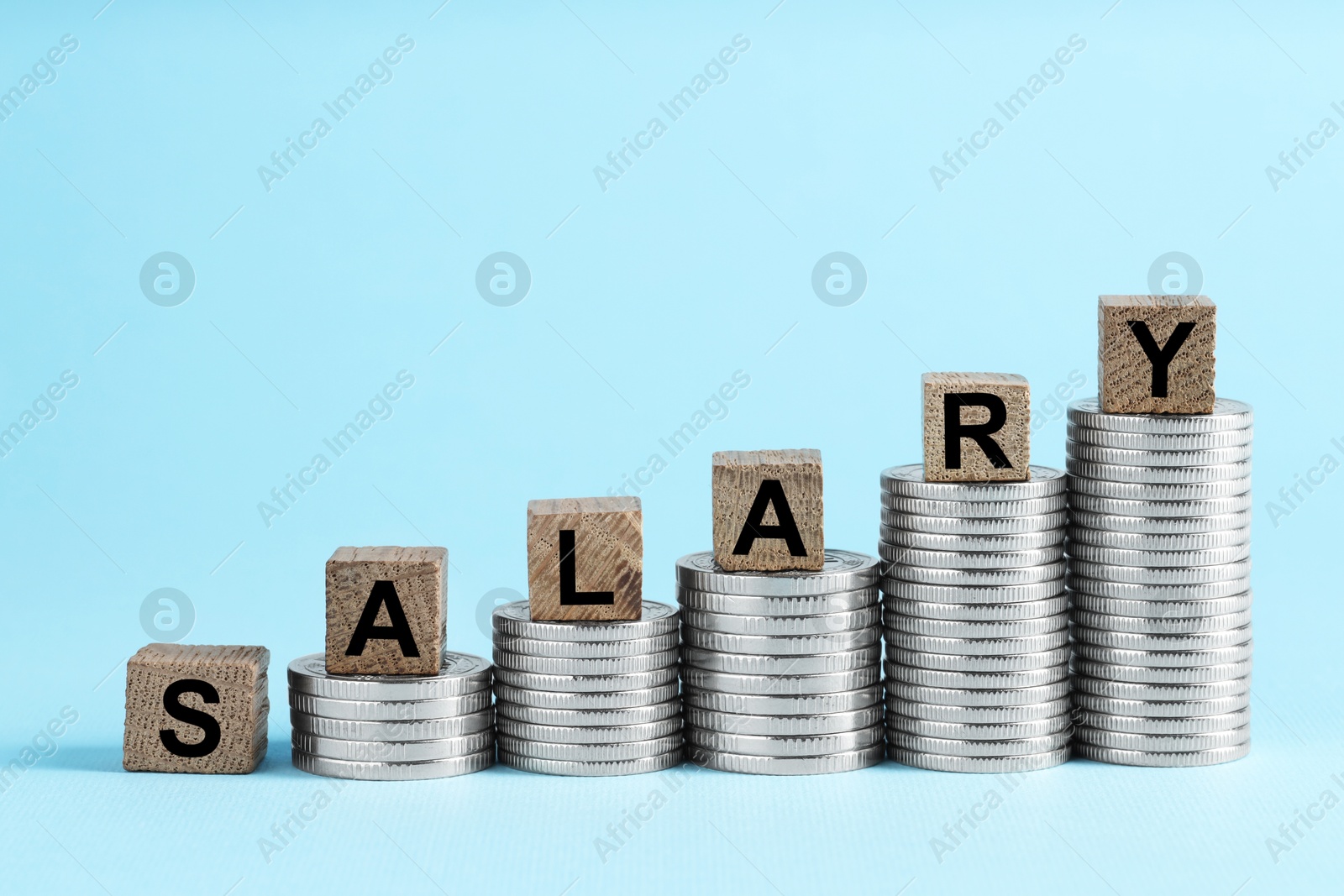 Photo of Word Salary made of wooden cubes and coins on light blue background, space for text