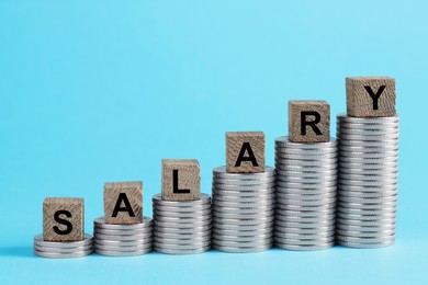 Photo of Word Salary made of wooden cubes and coins on light blue background, space for text