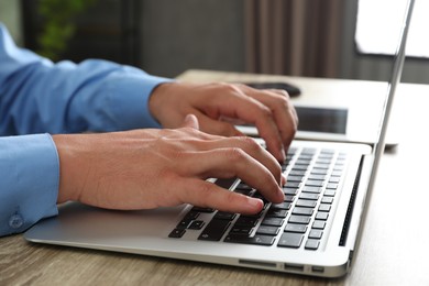 Photo of Businessman using laptop at wooden table, closeup. Modern technology