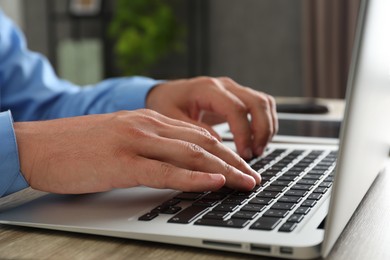 Photo of Businessman using laptop at wooden table, closeup. Modern technology