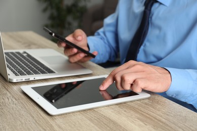 Photo of Businessman with smartphone, tablet and laptop at wooden table, closeup. Modern technology