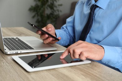 Photo of Businessman with smartphone, tablet and laptop at wooden table, closeup. Modern technology