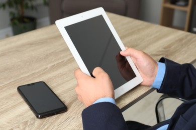 Photo of Businessman with tablet and smartphone at wooden table, closeup. Modern technology