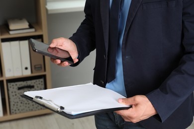 Photo of Businessman with clipboard using smartphone in office, closeup. Modern technology