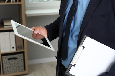 Photo of Businessman with clipboard using tablet in office, closeup. Modern technology