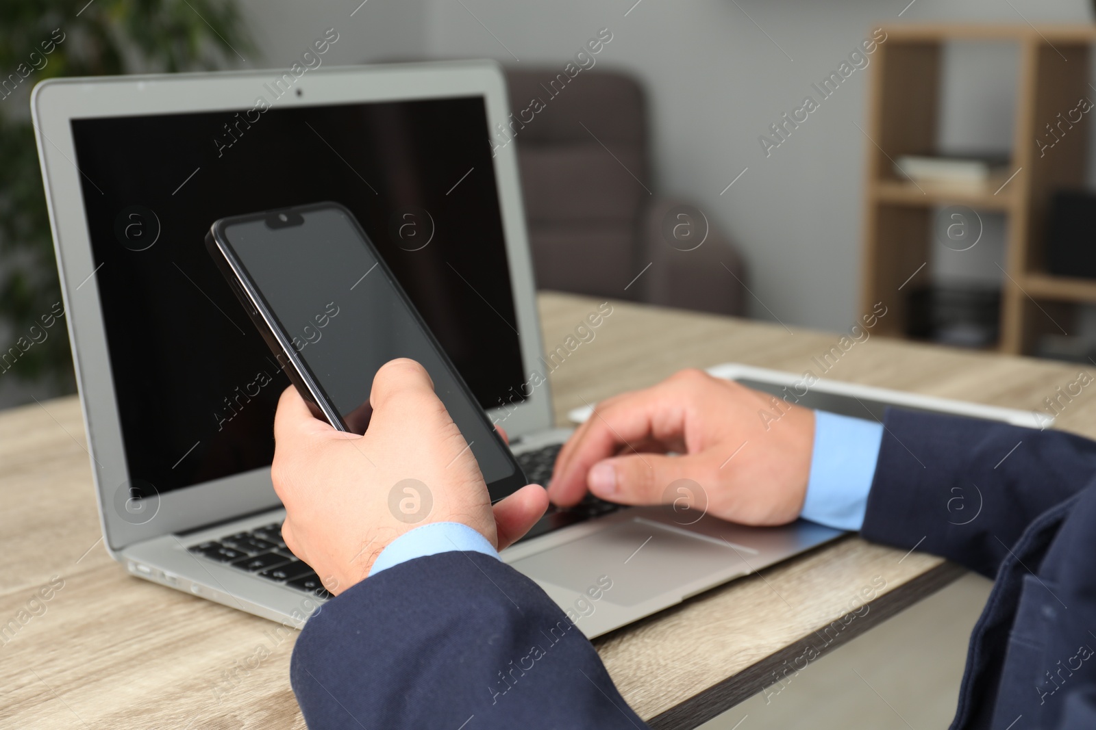 Photo of Businessman using smartphone and laptop at wooden table, closeup. Modern technology