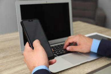 Photo of Businessman using smartphone and laptop at wooden table, closeup. Modern technology