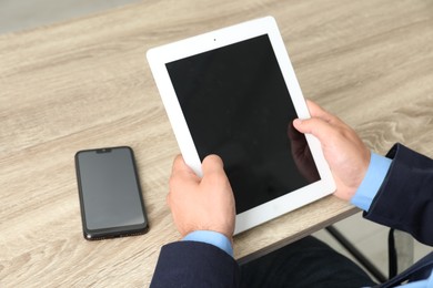 Photo of Businessman with tablet and smartphone at wooden table, closeup. Modern technology