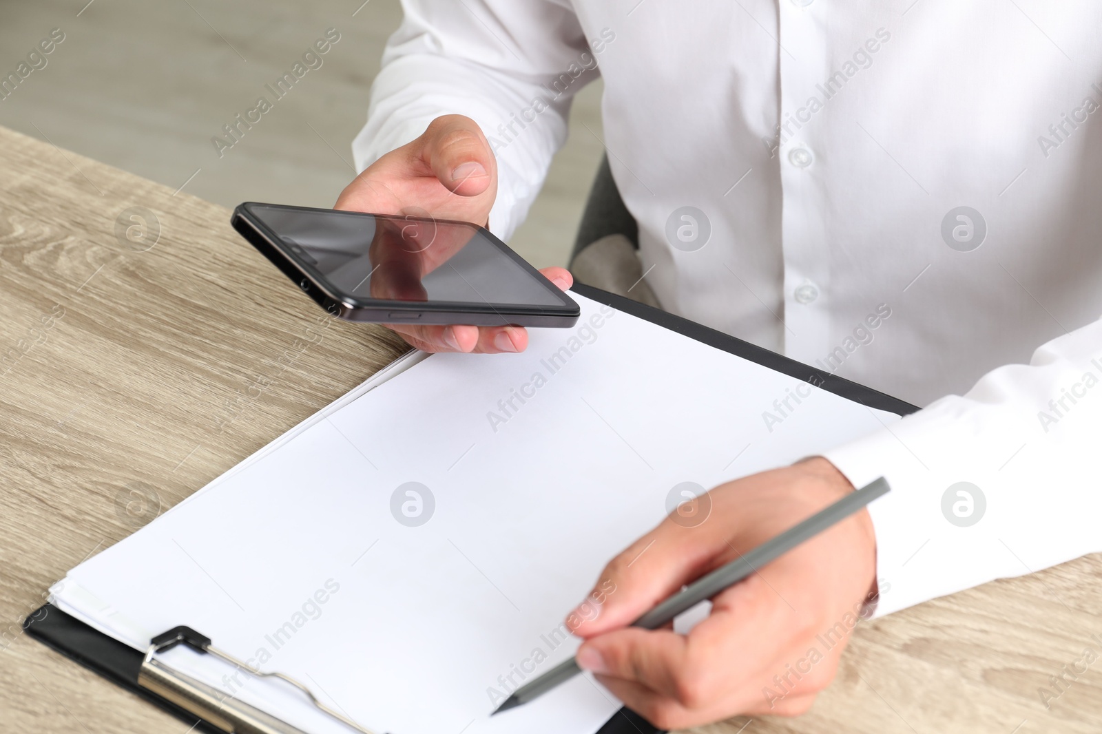 Photo of Businessman using smartphone while working at wooden table, closeup. Modern technology