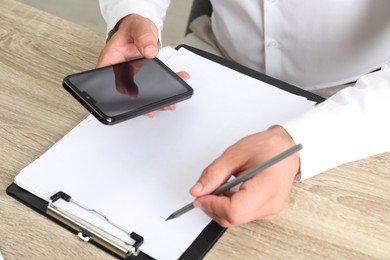 Photo of Businessman using smartphone while working at wooden table, closeup. Modern technology