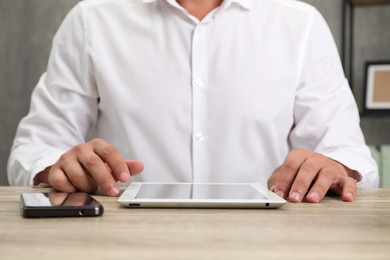 Photo of Businessman with tablet and smartphone at wooden table, closeup. Modern technology