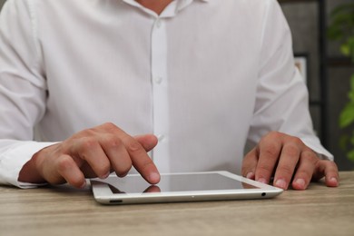 Photo of Businessman using tablet at wooden table, closeup. Modern technology