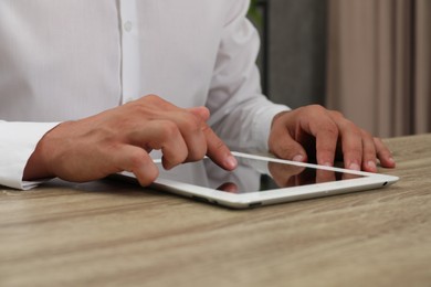 Photo of Businessman using tablet at wooden table, closeup. Modern technology