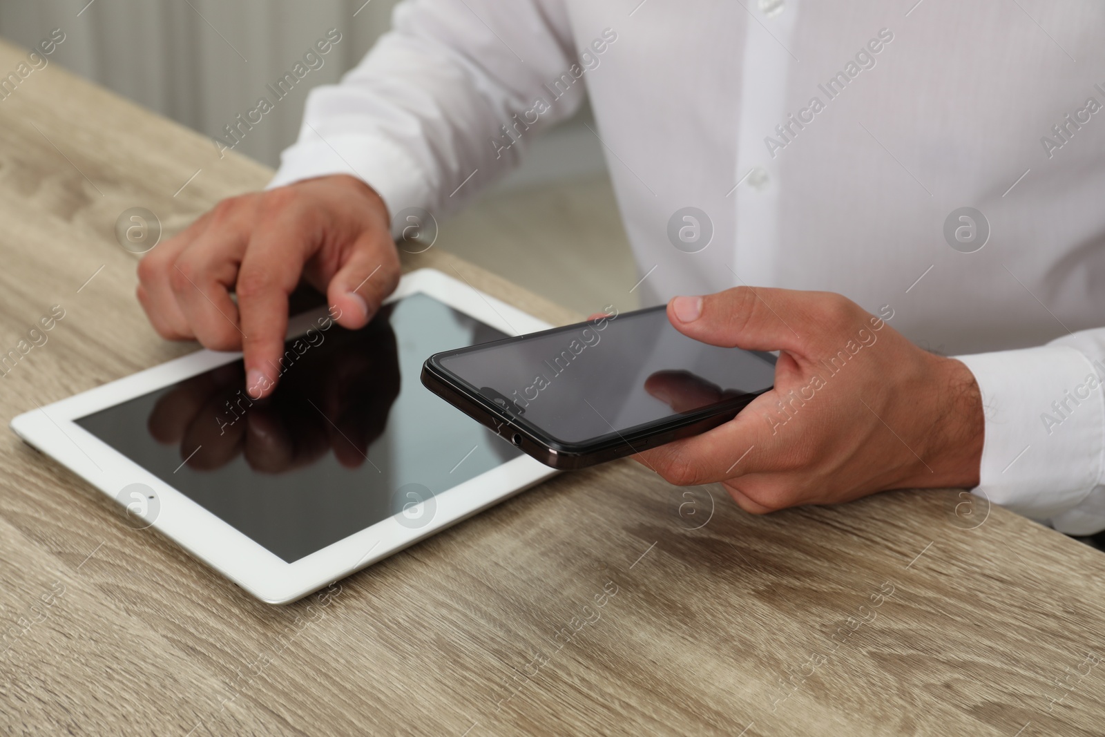 Photo of Businessman with smartphone and tablet at wooden table, closeup. Modern technology