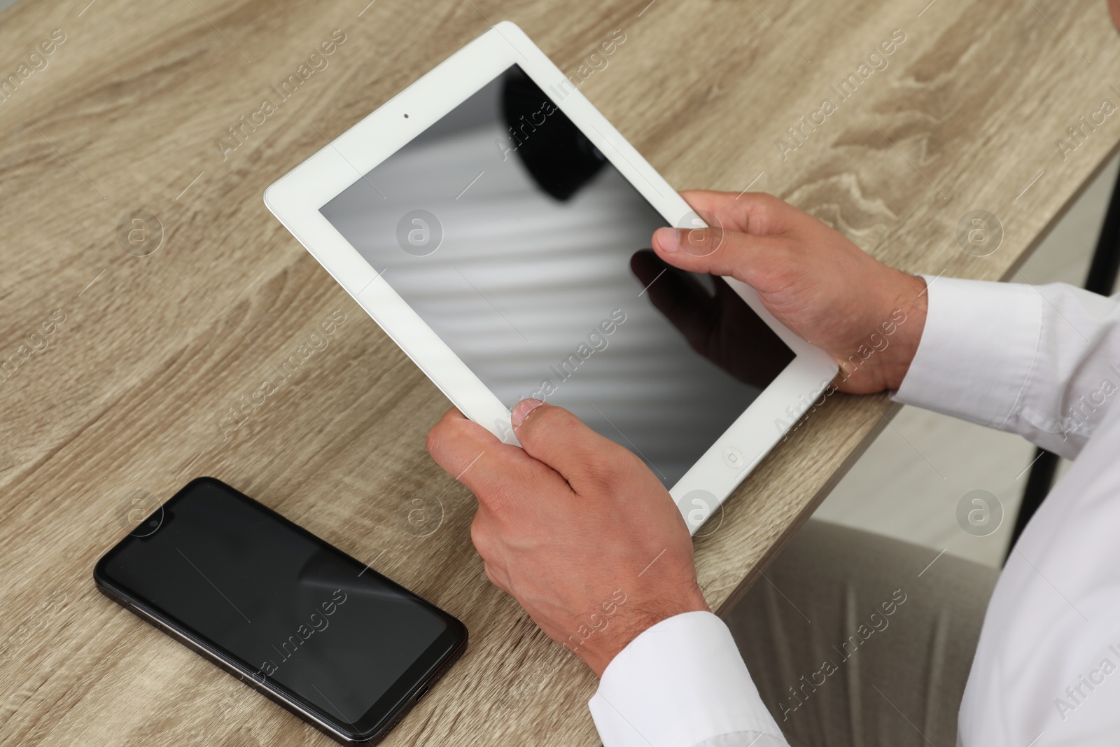 Photo of Businessman with tablet and smartphone at wooden table, closeup. Modern technology