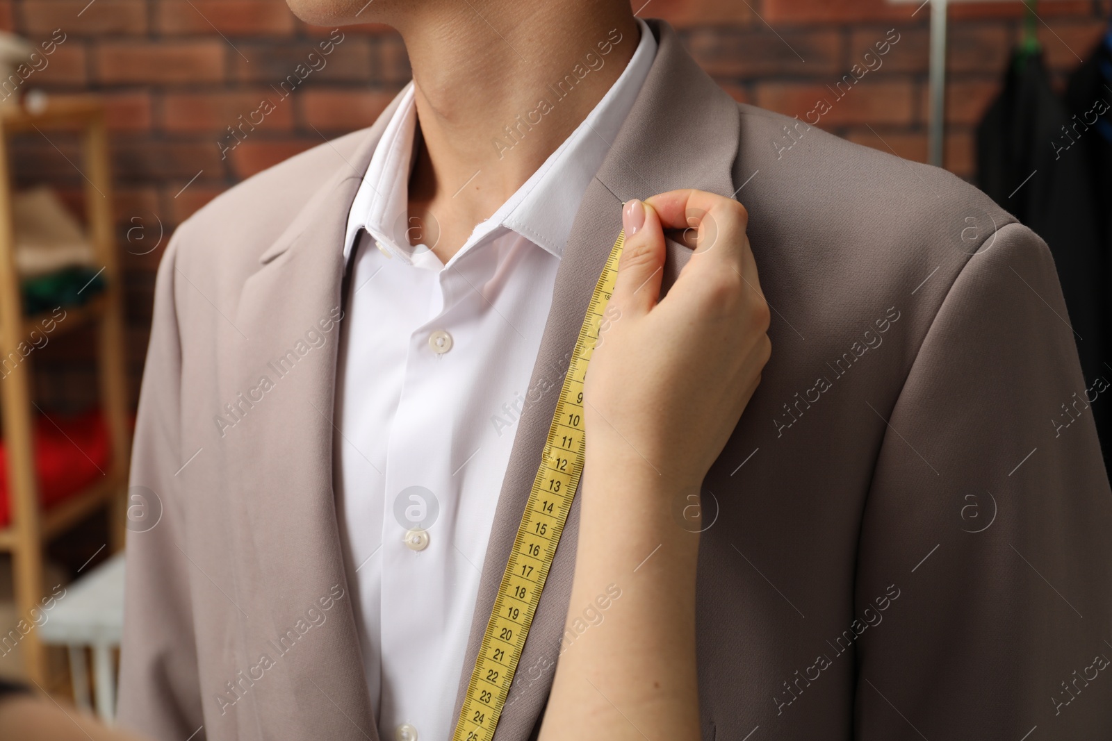 Photo of Professional tailor measuring jacket lapel on client in atelier, closeup