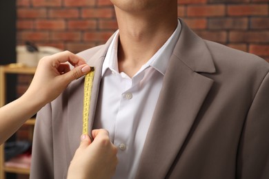 Photo of Professional tailor measuring jacket lapel on client in atelier, closeup