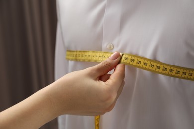 Professional tailor measuring client's chest circumference in atelier, closeup