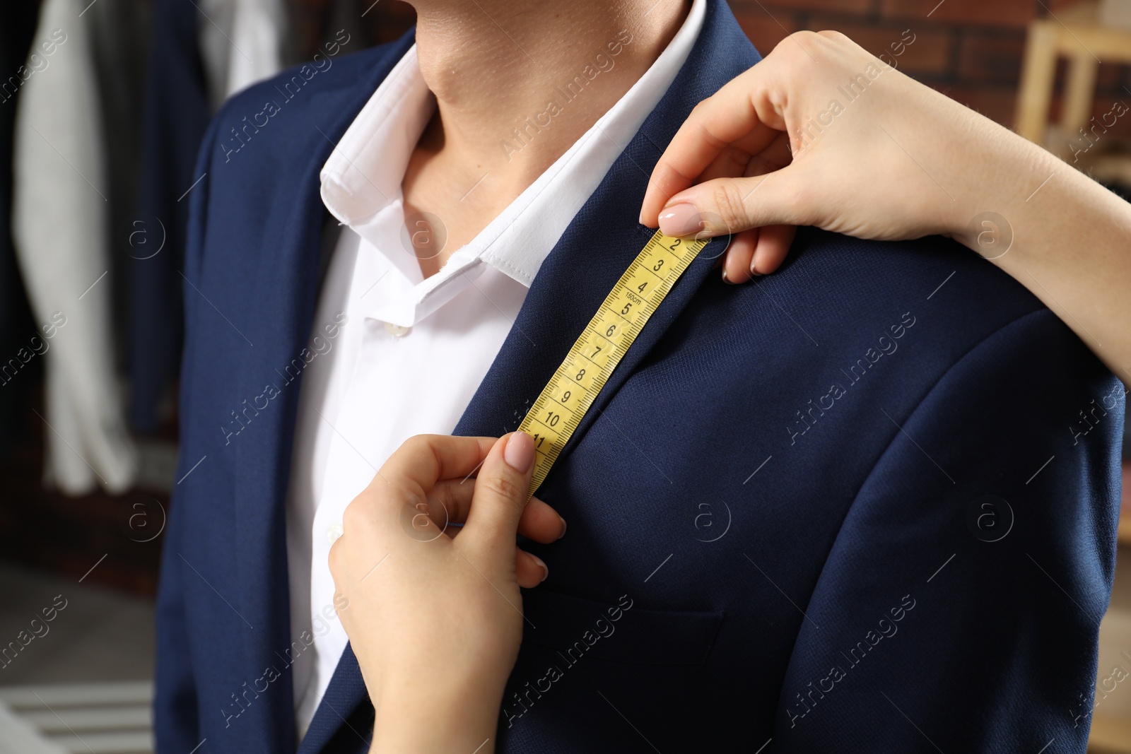 Photo of Professional tailor measuring jacket lapel on client in atelier, closeup