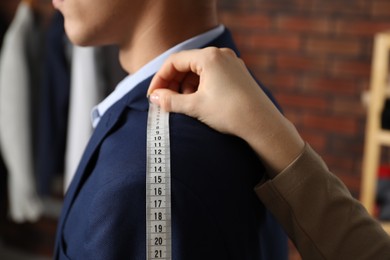 Photo of Professional tailor measuring shoulder seam length on client's jacket in atelier, closeup