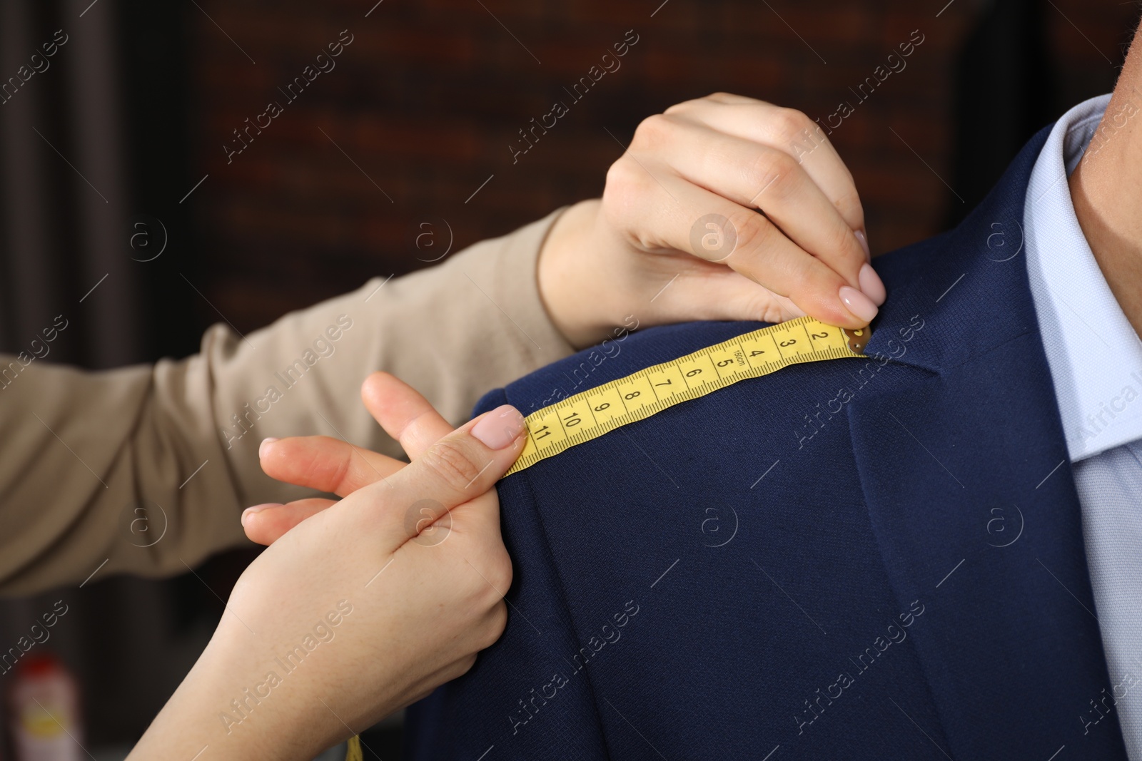 Photo of Professional tailor measuring shoulder seam length on client's jacket in atelier, closeup