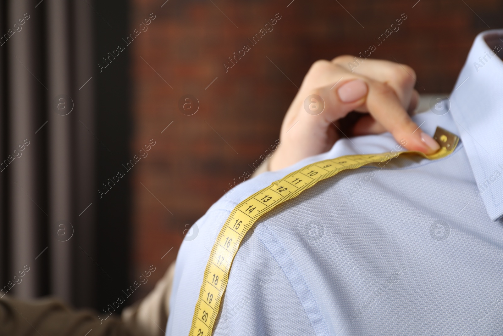 Photo of Professional tailor measuring shoulder seam length on client's shirt in atelier, closeup