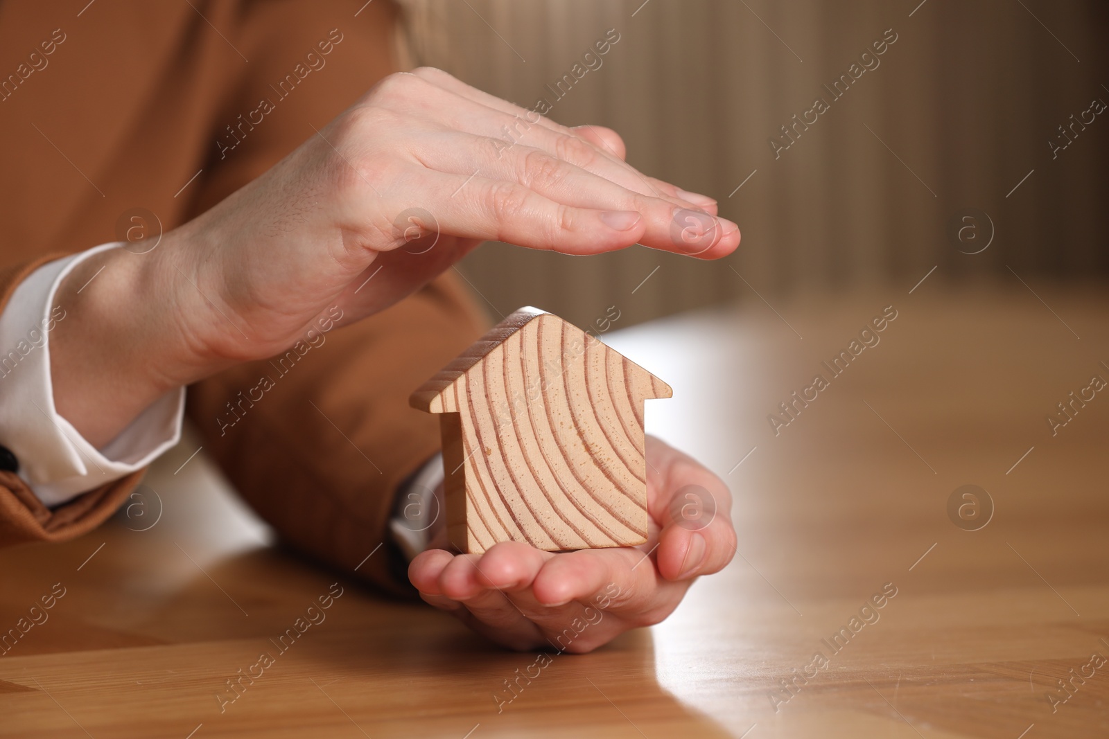 Photo of Property insurance. Real estate agent protecting house figure at wooden table, closeup