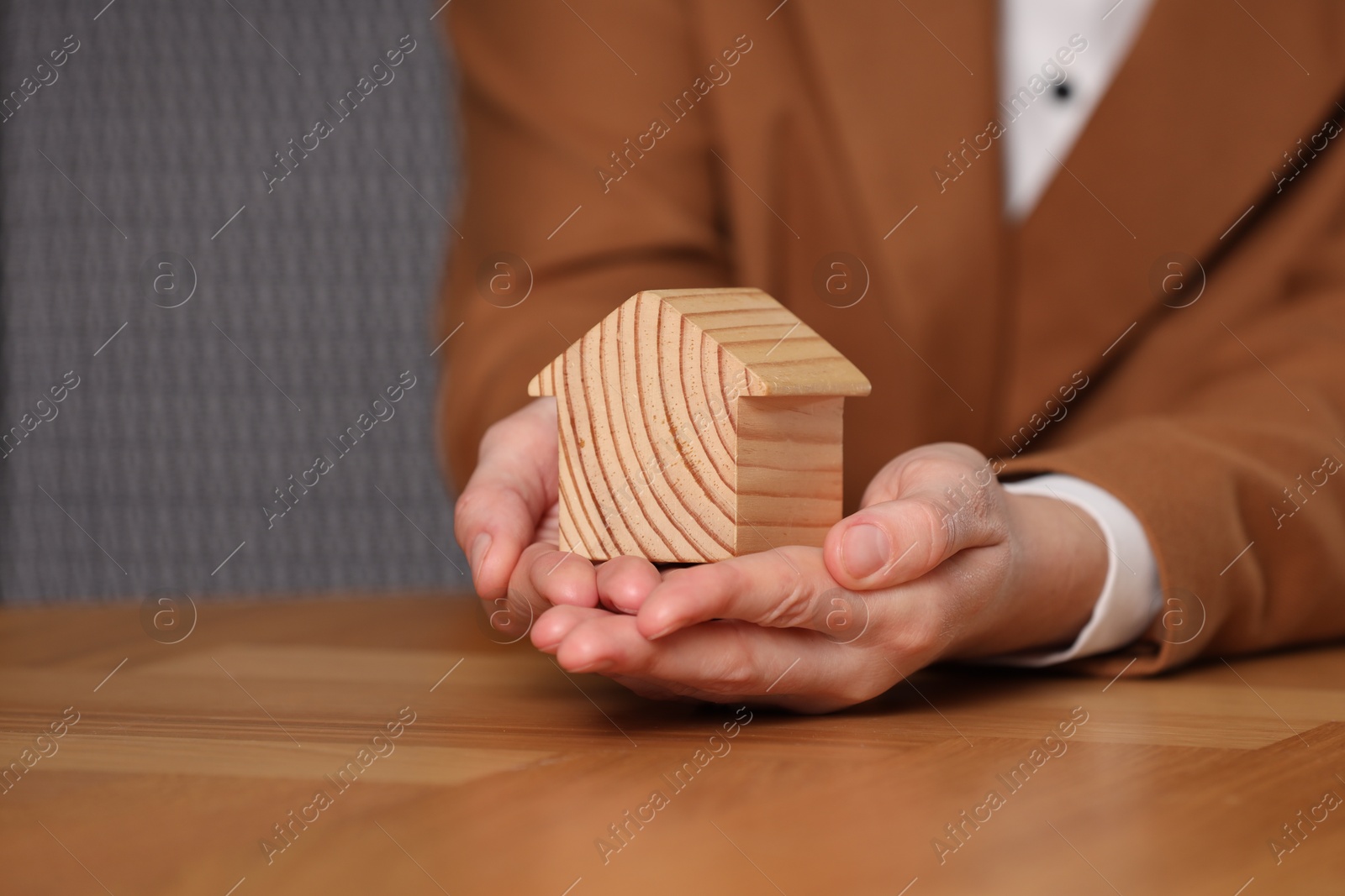 Photo of Property insurance. Real estate agent holding house figure at wooden table, closeup