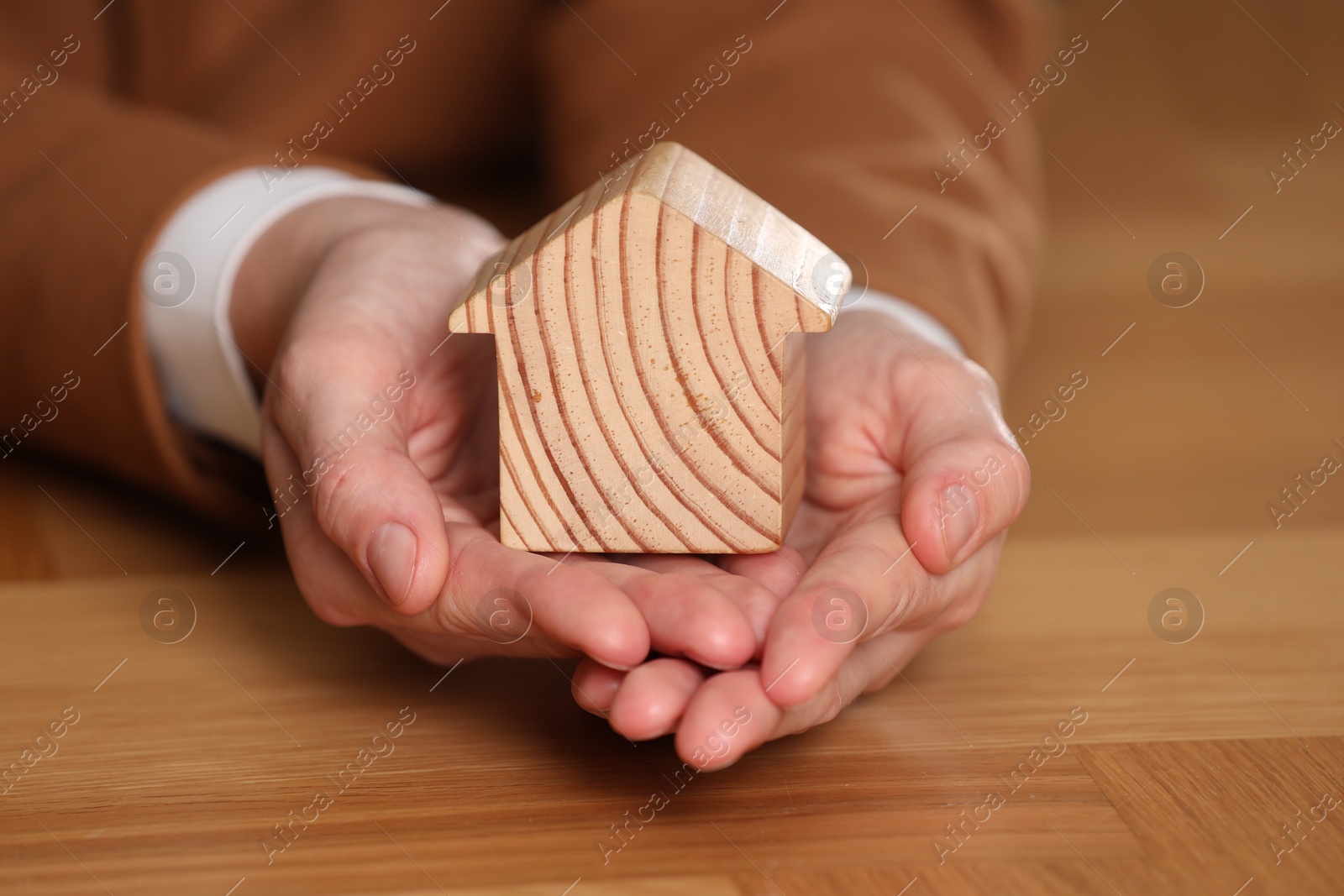 Photo of Property insurance. Real estate agent holding house figure at wooden table, closeup