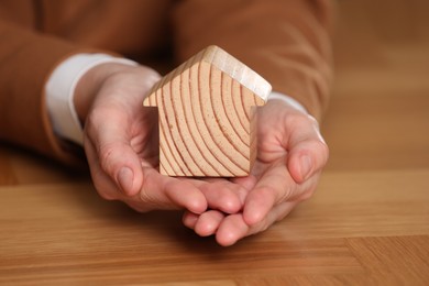 Photo of Property insurance. Real estate agent holding house figure at wooden table, closeup