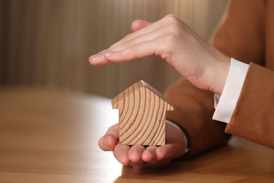 Photo of Property insurance. Real estate agent protecting house figure at wooden table, closeup