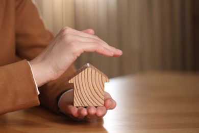 Photo of Property insurance. Real estate agent protecting house figure at wooden table, closeup