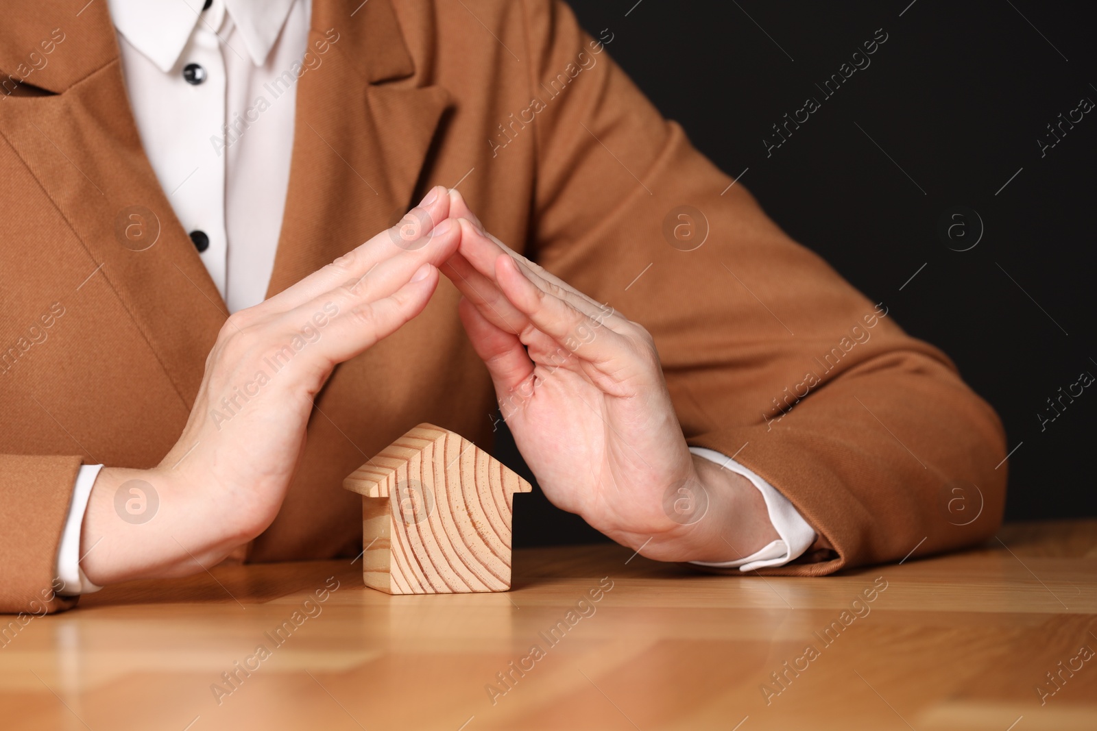 Photo of Property insurance. Real estate agent protecting house figure at wooden table, closeup