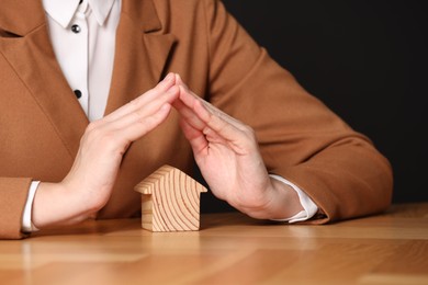 Photo of Property insurance. Real estate agent protecting house figure at wooden table, closeup