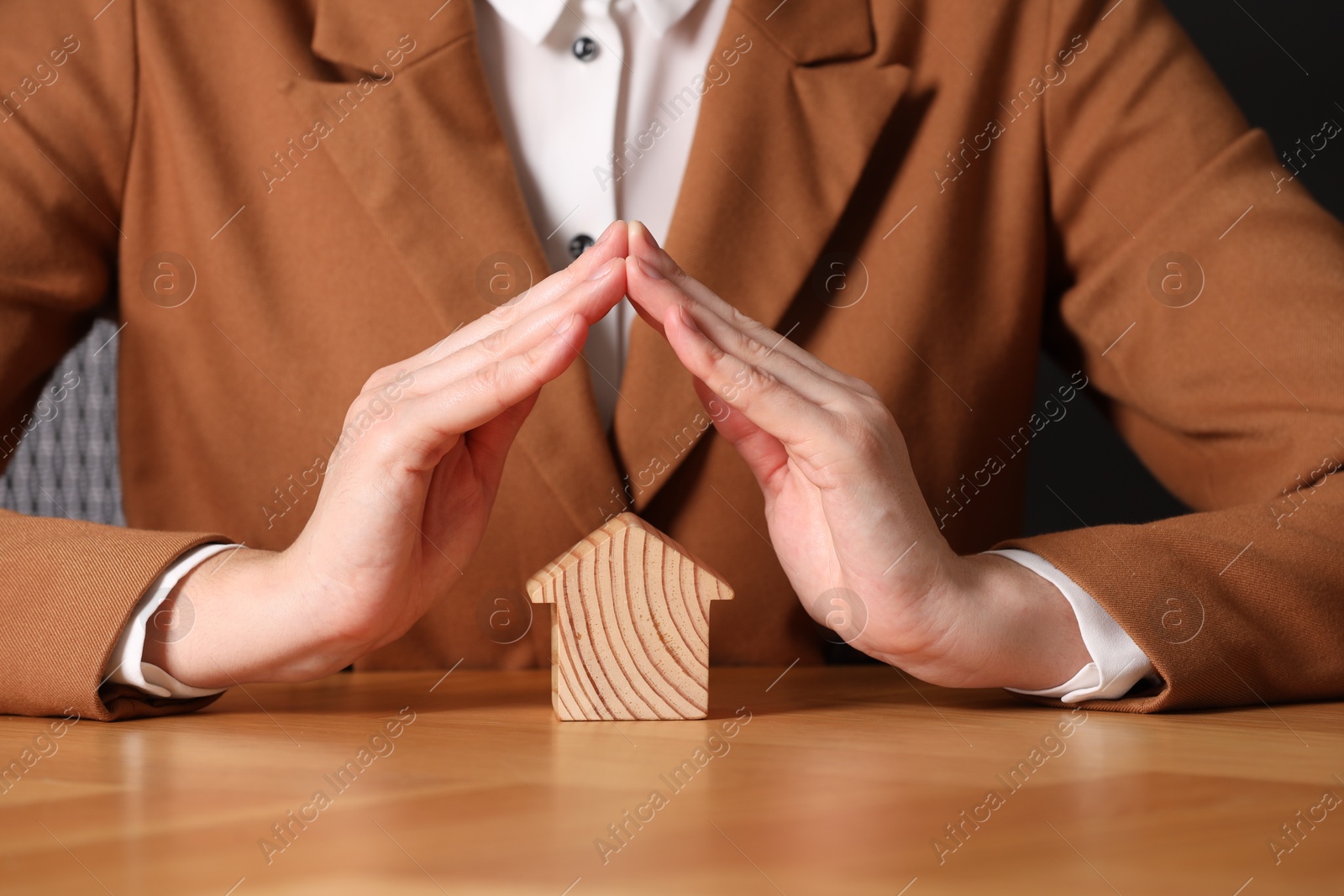 Photo of Property insurance. Real estate agent protecting house figure at wooden table, closeup