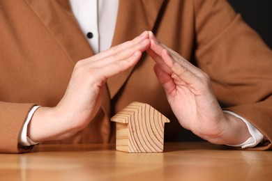 Photo of Property insurance. Real estate agent protecting house figure at wooden table, closeup