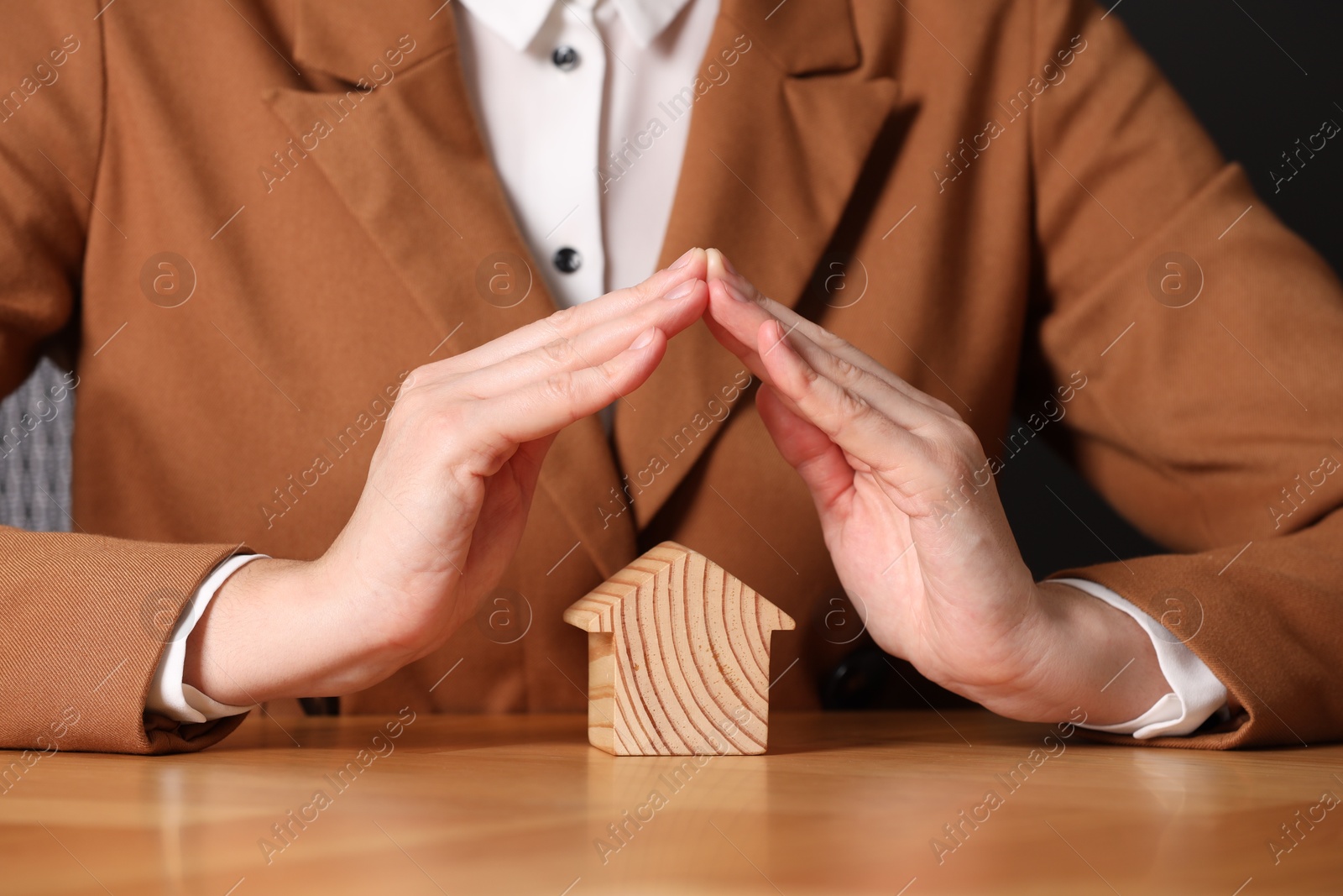 Photo of Property insurance. Real estate agent protecting house figure at wooden table, closeup