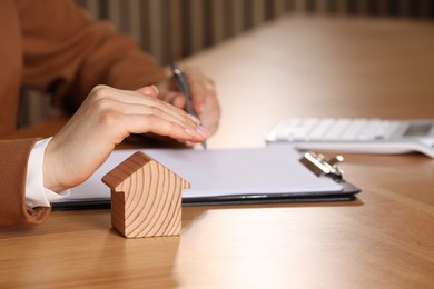 Photo of Property insurance. Real estate agent protecting house figure at wooden table, closeup