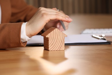 Photo of Property insurance. Real estate agent protecting house figure at wooden table, closeup