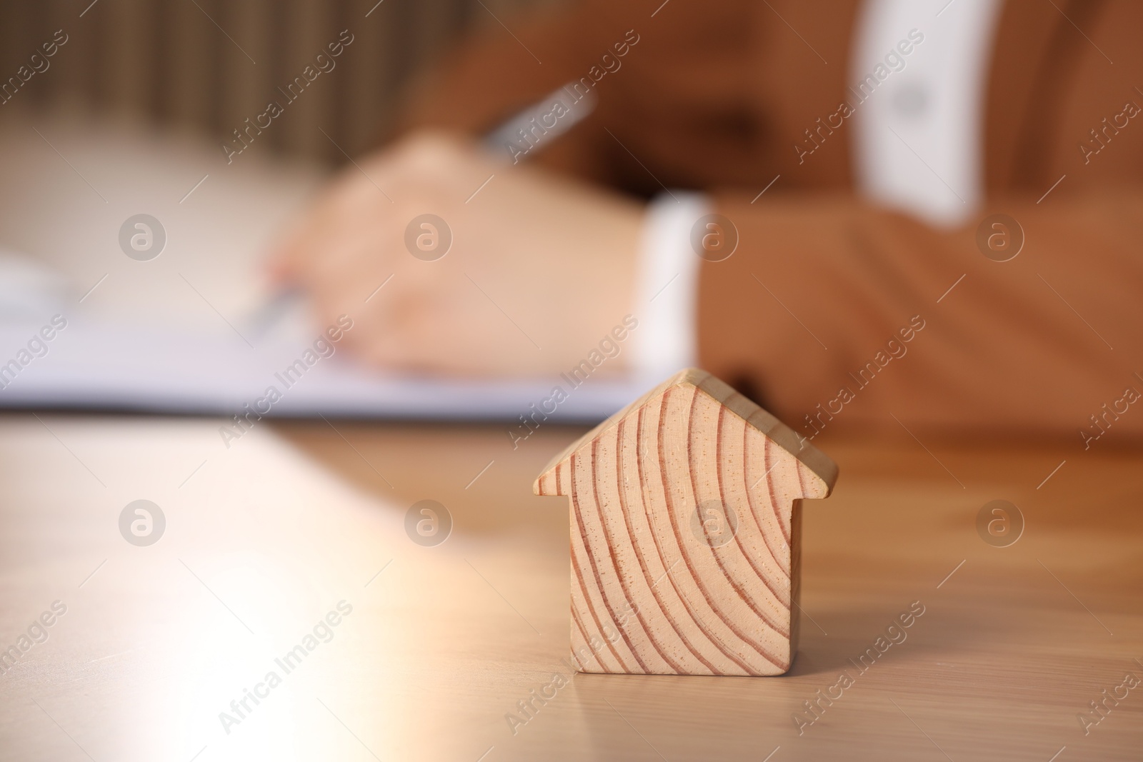 Photo of Property insurance. Real estate agent working at table indoors, focus on wooden house figure